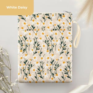 May include: Cream-coloured pouch with a daisy floral pattern. The embroidered design features white daisies with yellow centres and green stems. The pouch has a zip closure and a cream-coloured handle. The text "White Daisy" is in a yellow box.