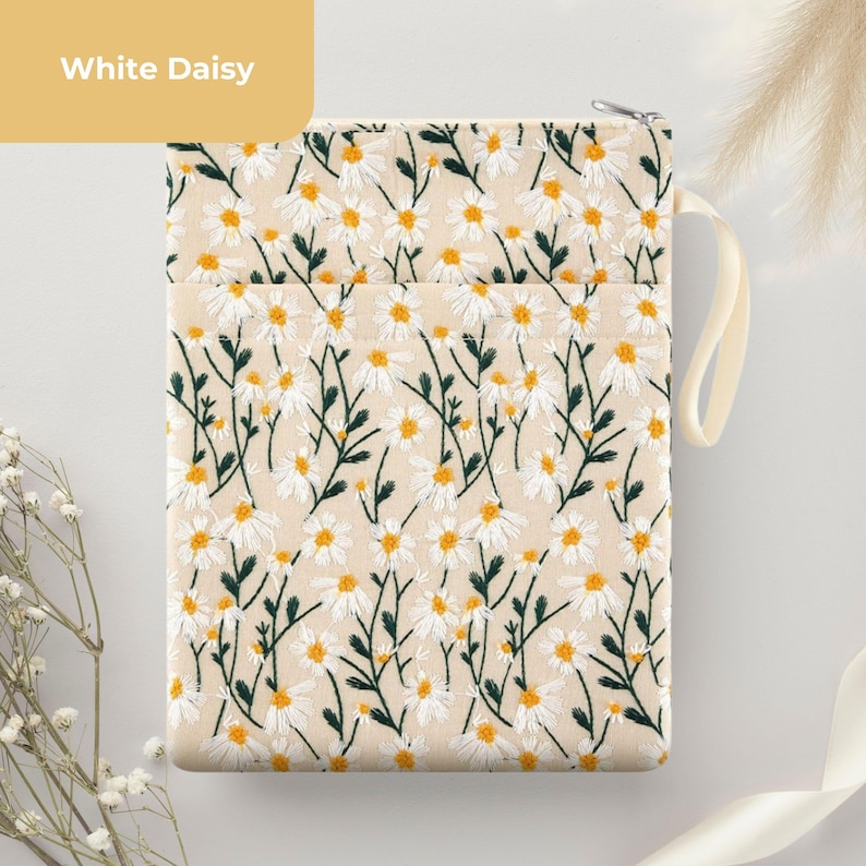 May include: Cream-coloured pouch with a daisy floral pattern. The embroidered design features white daisies with yellow centres and green stems. The pouch has a zip closure and a cream-coloured handle. The text "White Daisy" is in a yellow box.
