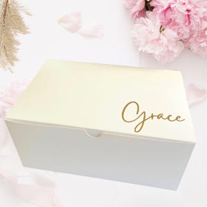 May include: A white gift box with a gold inscription that reads "Grace".