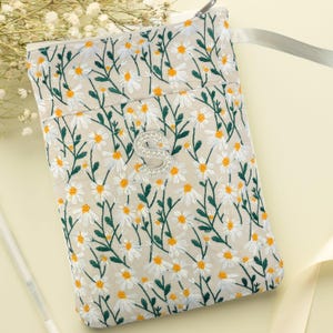 May include: A beige embroidered pouch with a daisy floral pattern. The pouch features white daisies with yellow centres and green stems. It has a silver zip and a rhinestone-studded silver initial "S". A light grey ribbon is attached.