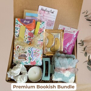May include: A gift box filled with a floral tote bag, Yogi tea, a reading list, eye patches, a candle, a hair clip, scrunchies, and fuzzy socks. The box is labeled "Premium Bookish Bundle".
