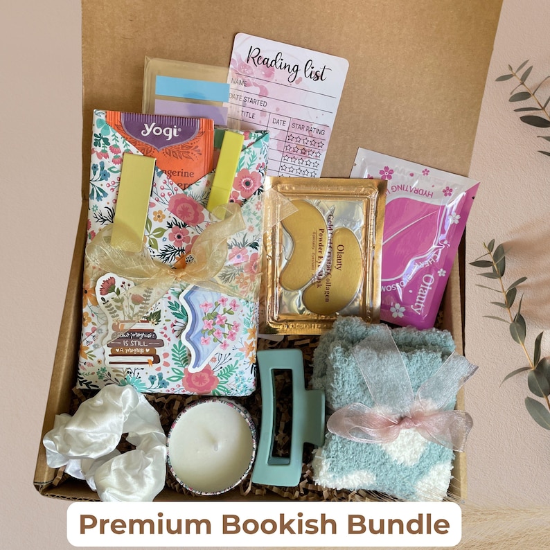 May include: A gift box filled with a floral tote bag, Yogi tea, a reading list, eye patches, a candle, a hair clip, scrunchies, and fuzzy socks. The box is labeled "Premium Bookish Bundle".