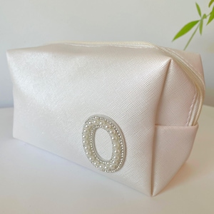 May include: A white satin cosmetic bag with a pearl and rhinestone embellishment in the shape of a circle.