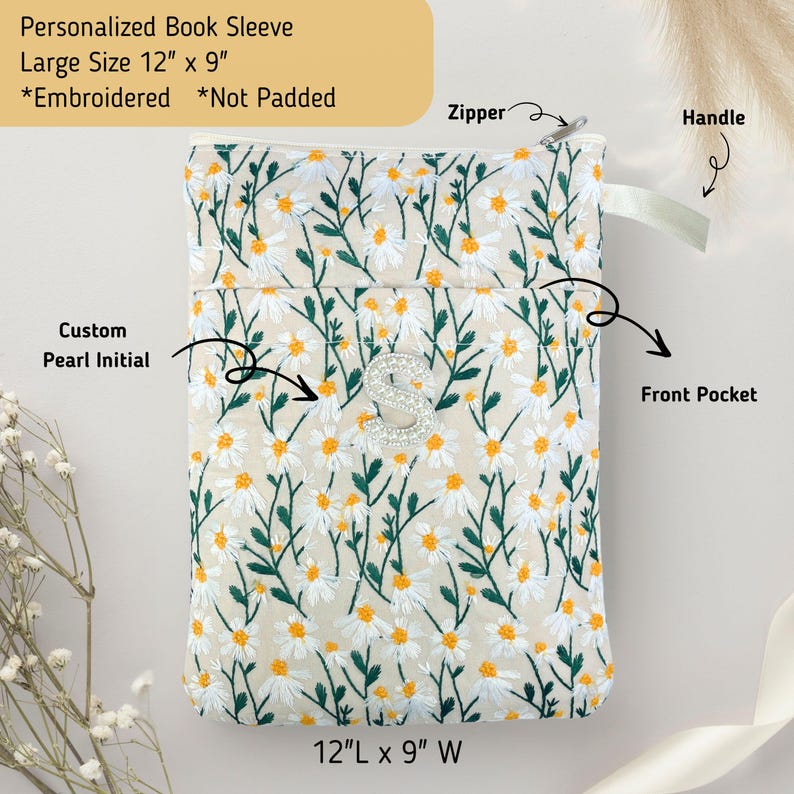 May include: Embroidered book sleeve with a daisy pattern, a custom pearl initial, and a front pocket. The sleeve is 30.5 cm long and 23 cm wide. Features a zipper and handle. The text reads: Personalized Book Sleeve, Large Size 12" x 9", *Embroidered *Not Padded.