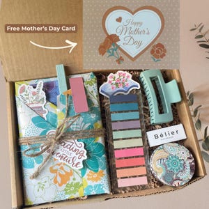 May include: A gift box with a floral-patterned book wrap tied with twine, a light blue hair clip, a compact mirror, and a set of colorful sticky notes. A Mother's Day card is included.