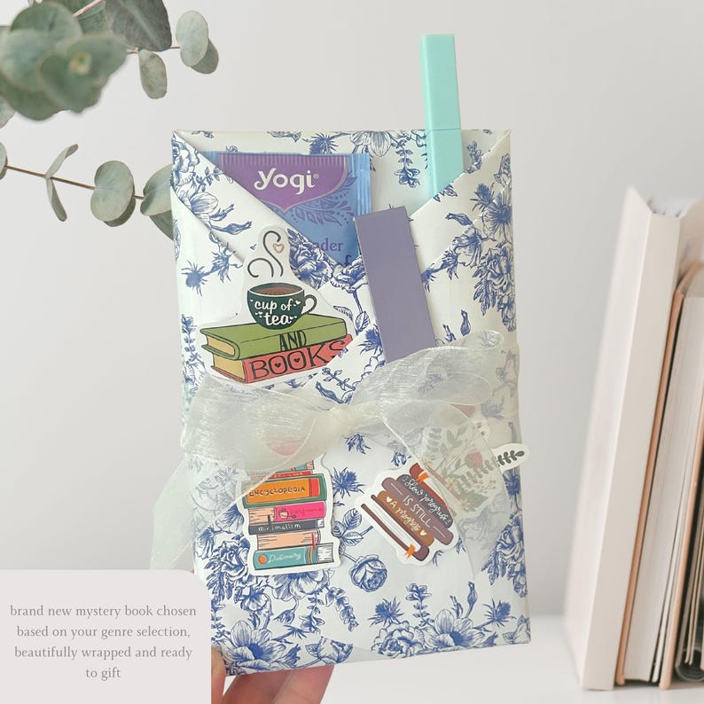 May include: A gift-wrapped package with a blue and white floral pattern, tied with a white ribbon. The package contains a tea bag, a bookmark, and a pen. Stickers with the words "cup of tea and books" and "books is still a romance" are visible.