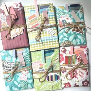 May include: An overhead shot of several wrapped books, each with a unique patterned paper cover. They are tied with twine and adorned with stickers and bookmarks. The stickers feature phrases like "Books & Dogs" and "Book Nerd."