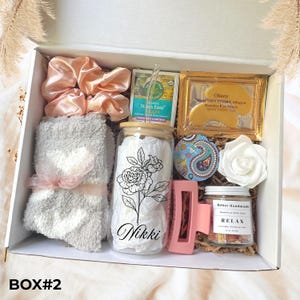 May include: A gift box filled with self-care items. Includes a glass with a floral design and the name "Nikki", a scrunchie, socks, tea, eye mask, bath salts, a hair clip, a decorative paisley coaster, and a white rose.