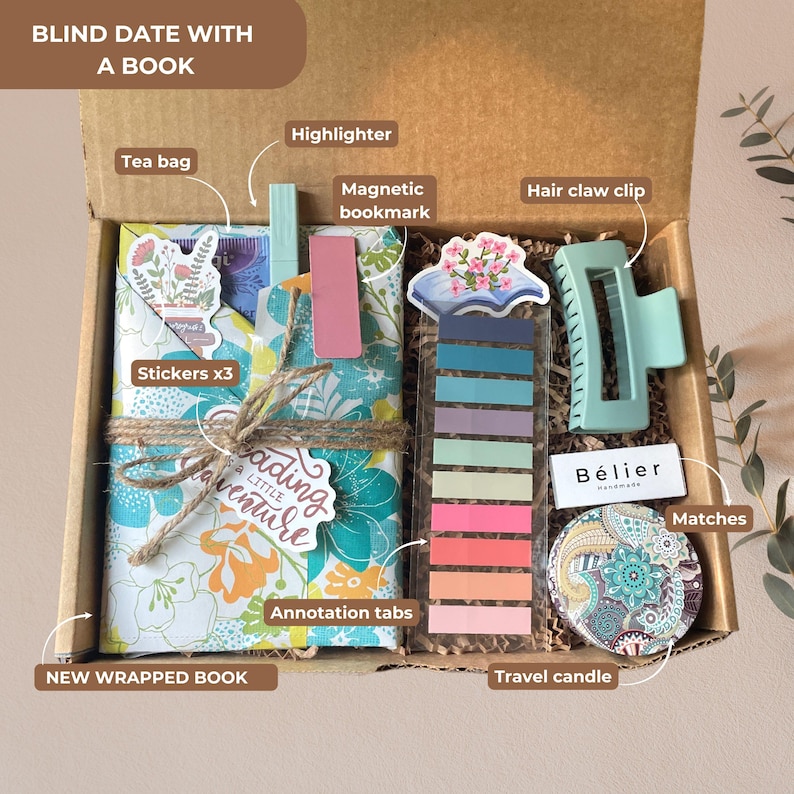 May include: A gift box labeled "Blind Date With A Book" contains a wrapped book, stickers, a highlighter, a magnetic bookmark, annotation tabs, a hair claw clip, a travel candle, matches, and a tea bag. The box is filled with decorative paper and twine.