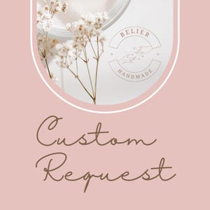 May include: A pink background with the text "Custom Request" in brown cursive writing. A white circle with a white outline contains a small bouquet of white flowers and a logo that says "Belier Handmade" with a stylized image of two hands reaching towards each other.
