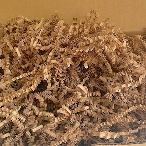 May include: Brown paper shred filling a cardboard box. The shred is made of thin, crinkled strips of paper.