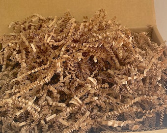 May include: Brown paper shred filling a cardboard box. The shred is made of thin, crinkled strips of paper.