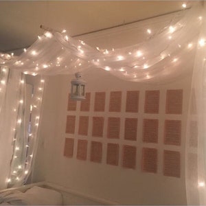 May include: White sheer curtains with string lights draped over them, creating a canopy effect. A small white lantern hangs from the center of the canopy.