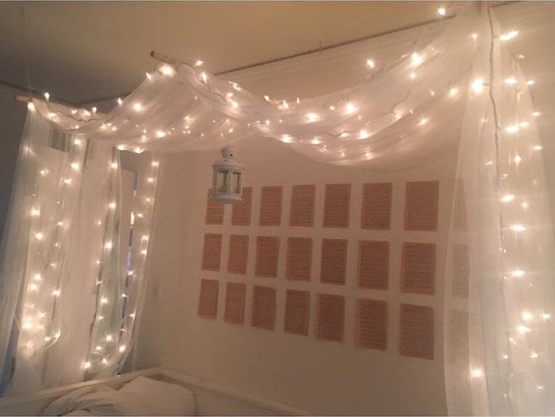 May include: White sheer curtains with string lights draped over them, creating a canopy effect. A small white lantern hangs from the center of the canopy.