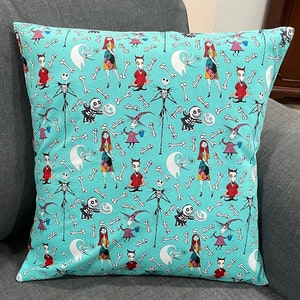 May include: A turquoise pillowcase with a repeating pattern of characters from the Nightmare Before Christmas. The characters include Jack Skellington, Sally, and Oogie Boogie. The pattern also includes bones and other Halloween-themed imagery.
