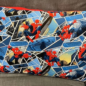 May include: A blue and red pillow with a repeating pattern of Spiderman swinging through a city skyline. The background is a blue and black web pattern.