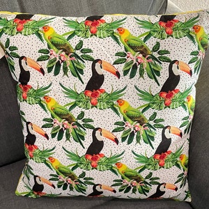 May include: A white throw pillow with a tropical print featuring toucans and parrots. The pillow has a yellow border and a white background with black polka dots.