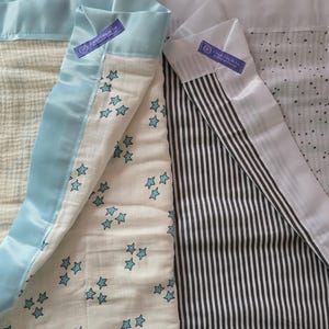 May include: Baby blankets with various patterns. One blanket features a cream-colored fabric with blue stars, another has black and white stripes, and a third has a cream-colored fabric with small black dots. Each blanket is trimmed with a light blue satin border.
