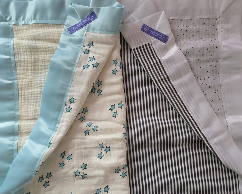 May include: Baby blankets with various patterns. One blanket features a cream-colored fabric with blue stars, another has black and white stripes, and a third has a cream-colored fabric with small black dots. Each blanket is trimmed with a light blue satin border.