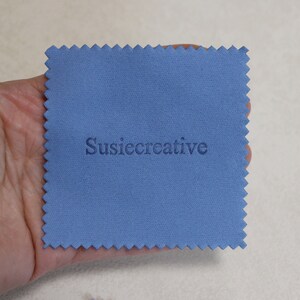 May include: A blue microfiber cleaning cloth with the text "SusieCreative" printed in white.