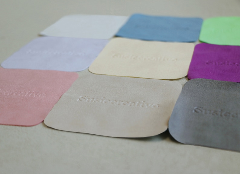 Puede incluir: Nueve muestras cuadradas de diferentes materiales, incluyendo gamuza, cuero y tela. Cada muestra tiene un color y una textura diferentes, y la palabra "Sustentare" est&aacute; grabada en relieve en cada muestra.