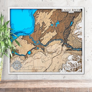 Puede incluir: Un mapa de madera enmarcado de Eagle River, Alaska, con un borde blanco. El mapa presenta un diseño topográfico detallado con tonos de marrón, azul y beige. Una rosa de los vientos está en la esquina inferior izquierda, y el texto "EAGLE RIVER Alaska" está en la parte superior.