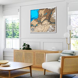 May include: A framed wooden map of Eagle River, with a detailed relief of the terrain. The map features shades of blue for water and brown for land, with the text "EAGLE RIVER" at the top. The artwork is displayed in a bright, modern living room.