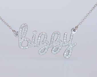 Op de afbeelding: Een zilverkleurige ketting met een naamhanger in cursief schrift die het woord "bizzy" vormt. Het gehele oppervlak van de letters is ingelegd met kleine, heldere, fonkelende steentjes en bevestigd aan een fijne ketting.