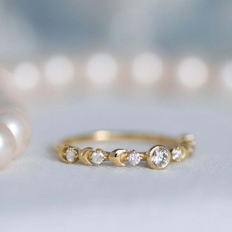 K&ouml;nnte beinhalten: Ein zarter Goldring mit einem Halbmond-Design und kleinen Diamanten. Der Ring hat einen gr&ouml;&szlig;eren runden Diamanten in der Mitte.