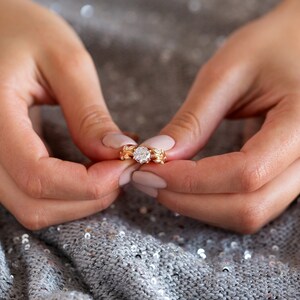 May include: A close-up of a hand wearing a gold ring with a large, clear diamond. The ring is set in a delicate, floral design.