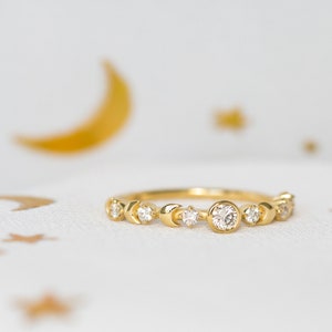 K&ouml;nnte beinhalten: Ein goldener Ring mit einem Halbmond-Design und kleinen Diamanten. Der Ring liegt auf einem wei&szlig;en Hintergrund mit goldenen Sternen.