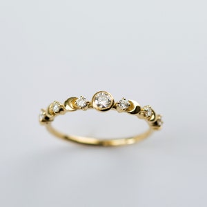 K&ouml;nnte beinhalten: Ein zarter Goldring mit einem Halbmond-Design und kleinen Diamanten, die in das Metall gefasst sind. Der Ring hat einen gr&ouml;&szlig;eren runden Diamanten in der Mitte.