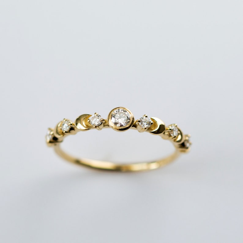 K&ouml;nnte beinhalten: Ein zarter Goldring mit einem Halbmond-Design und kleinen Diamanten, die in das Metall gefasst sind. Der Ring hat einen gr&ouml;&szlig;eren runden Diamanten in der Mitte.