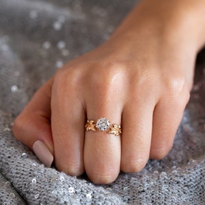 May include: A gold ring featuring a large, round, clear diamond set in a delicate, leaf-shaped design.