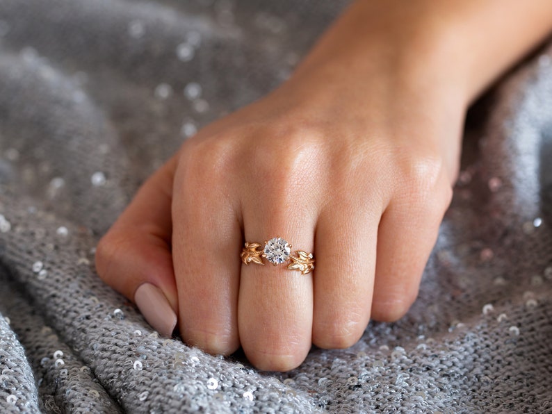 May include: A gold ring featuring a large, round, clear diamond set in a delicate, leaf-shaped design.