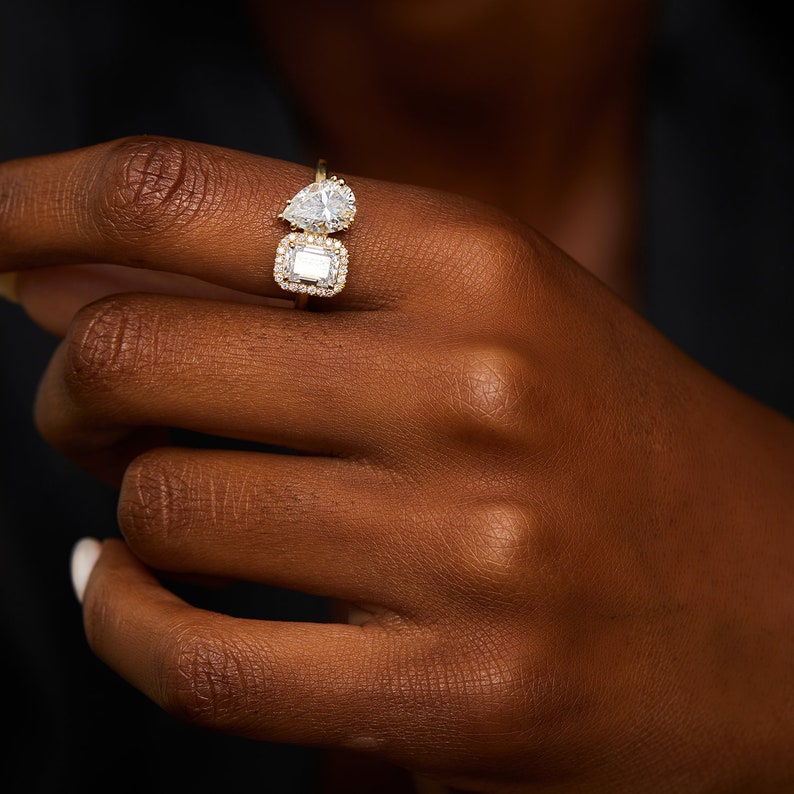 This is a stunning double-stone engagement ring, the perfect two-stone diamond ring, set with pear and emerald cut moissanite, surrounded by a halo of white diamonds, a unique toi et moi engagement ring.