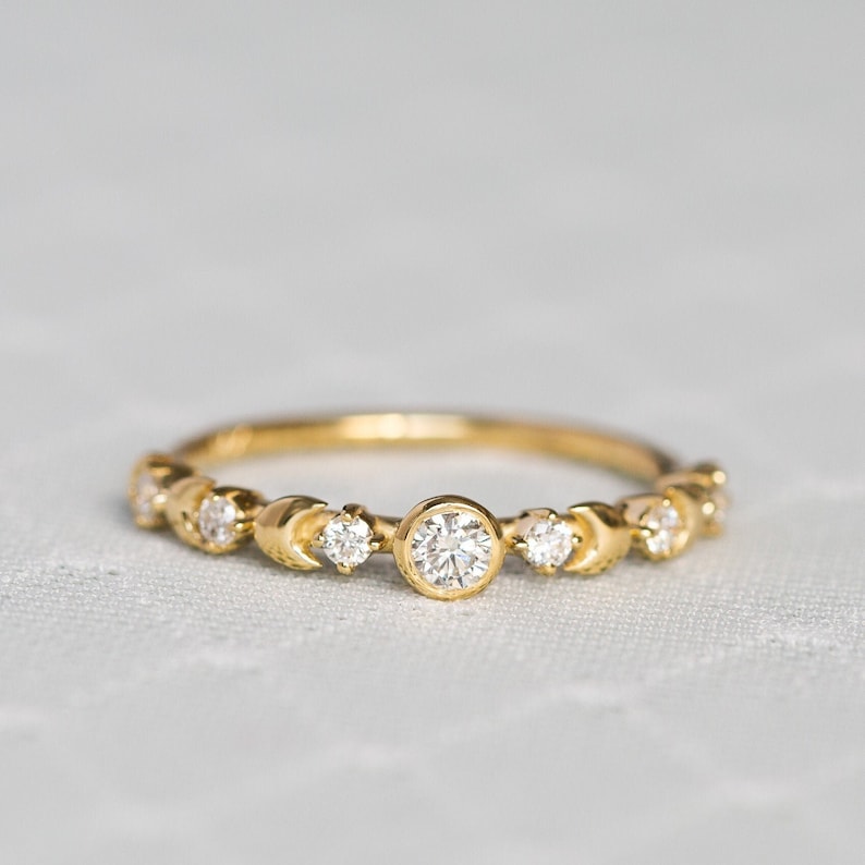 K&ouml;nnte beinhalten: Ein zarter Goldring mit einer Reihe kleiner Diamanten und einem gr&ouml;&szlig;eren runden Diamanten in der Mitte.