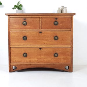 May include: A wooden chest of drawers with four drawers. The chest is made of light brown wood and has brass-coloured knobs. The bottom of the chest has a curved design. The chest is a piece of furniture.