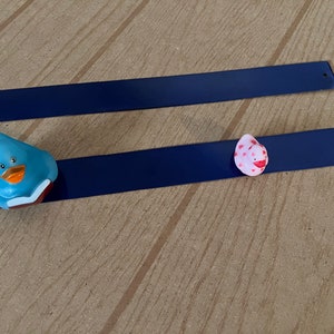 Puede incluir: Dos tiras magn&eacute;ticas azules con un pato azul y un pato rosa con lunares rojos en la parte superior.