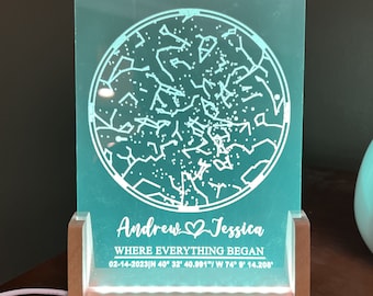 May include: A teal blue illuminated star map with a white wooden base. The star map shows the constellations visible on February 14, 2023 at 40° 32' 40.991" N, 74° 9' 14.208' W. The text "Andrew Jessica Where Everything Began" is engraved below the star map.