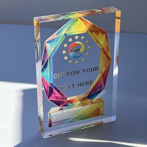 May include: A clear acrylic trophy with a colorful geometric design. The trophy features the text "CUSTOM YOUR TEXT HERE" and a logo. The design incorporates gold, blue, yellow, and red hues. The trophy has a rectangular shape and a gold base.
