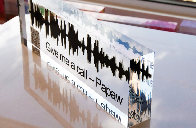 May include: A clear acrylic block with a black sound wave graphic and the text "Give me a call - Papaw" inscribed on the front. The text is reflected on the bottom of the block.
