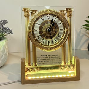 May include: A gold-coloured clock with Roman numerals on a glass plaque with a wooden base. The plaque has a message that reads "Happy Retirement! Wishing you endless joy and fulfillment in this new chapter of life. May your days be filled with happiness, health, and relaxation. Cheers to all the wonderful moments ahead." The plaque also has a space for a name.