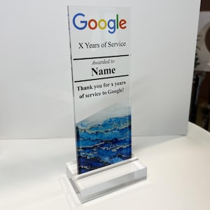 Puede incluir: Una placa de premio de acr&iacute;lico transparente con el logotipo de Google y el texto "X Years of Service" y "Awarded to Name". La placa tambi&eacute;n incluye el texto "Thank you for x years of service to Google!" y un dise&ntilde;o abstracto azul y blanco.