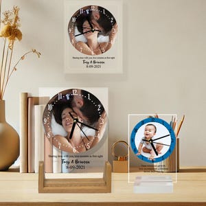 May include: Two glass clocks with custom photos and text. The first clock features a couple in bed, with the text "Sharing time with you, love remains as first sight Tony & Brianna 8-09-2021". The second clock features a baby, with the text "Time witnesses love accompanies a lifetime 04-04-2077".