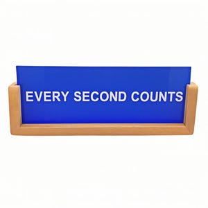 May include: A rectangular sign with the text "EVERY SECOND COUNTS" in white letters on a blue background. The sign is held in a light brown wooden frame.