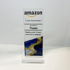 Puede incluir: Una placa de premio de acr&iacute;lico transparente con un dise&ntilde;o abstracto azul y dorado. La placa tiene el logotipo de Amazon y el texto "5 year Amaversary!"  "Awarded to Name" y "Thank you for 5 years of service to Amazon!"