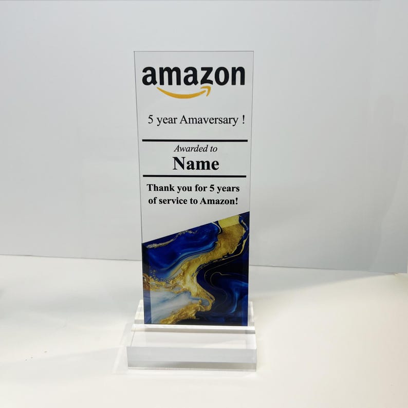 Puede incluir: Una placa de premio de acr&iacute;lico transparente con un dise&ntilde;o abstracto azul y dorado. La placa tiene el logotipo de Amazon y el texto "5 year Amaversary!"  "Awarded to Name" y "Thank you for 5 years of service to Amazon!"
