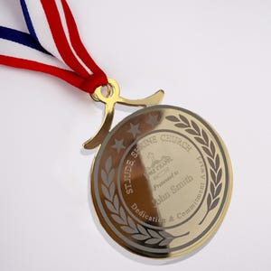 May include: A gold-colored medal with the text "St. Jude Shrine Church" and "Dedication & Commitment Award" is displayed. The medal is attached to a red, white, and blue ribbon. The medal is engraved with the name "John Smith".
