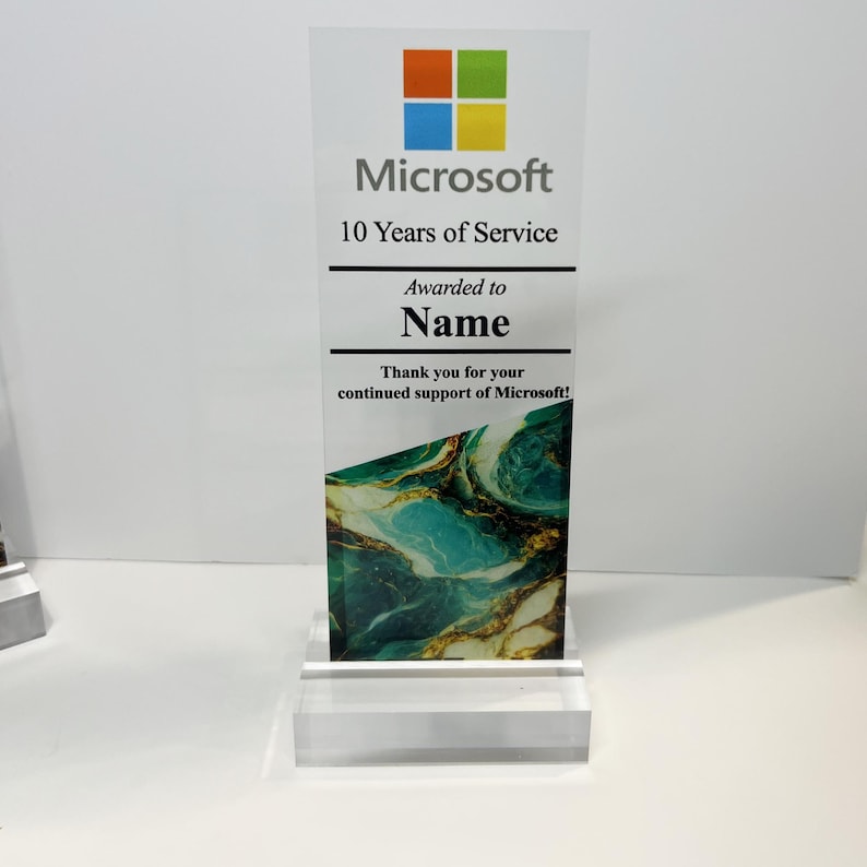Puede incluir: Una placa de premio de acr&iacute;lico transparente con un logotipo de Microsoft azul, verde y amarillo. La placa dice "Microsoft 10 Years of Service Awarded to Name Thank you for your continued support of Microsoft!" El fondo es un dise&ntilde;o abstracto verde y dorado.